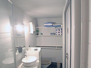 A compact bathroom with a toilet, sink, and shelves for toiletries. - Charming family apartment in central Saint-Vaast-la-Hougue with wifi (Saint-Vaast-la-Hougue)