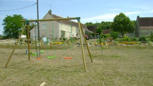 Une balançoire installée dans un espace herbeux, avec une maison en arrière-plan.