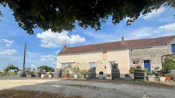 Un bâtiment rustique en pierre, doté d’un toit en tuiles, entouré de plantes en pot et bordé d’une allée en gravier.