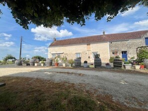 A rustic stone building with a tiled roof, surrounded by potted plants and a gravel driveway. - Cottage in Touraine: Countryside, 3 Bedrooms, Near Chenonceau (Chédigny)