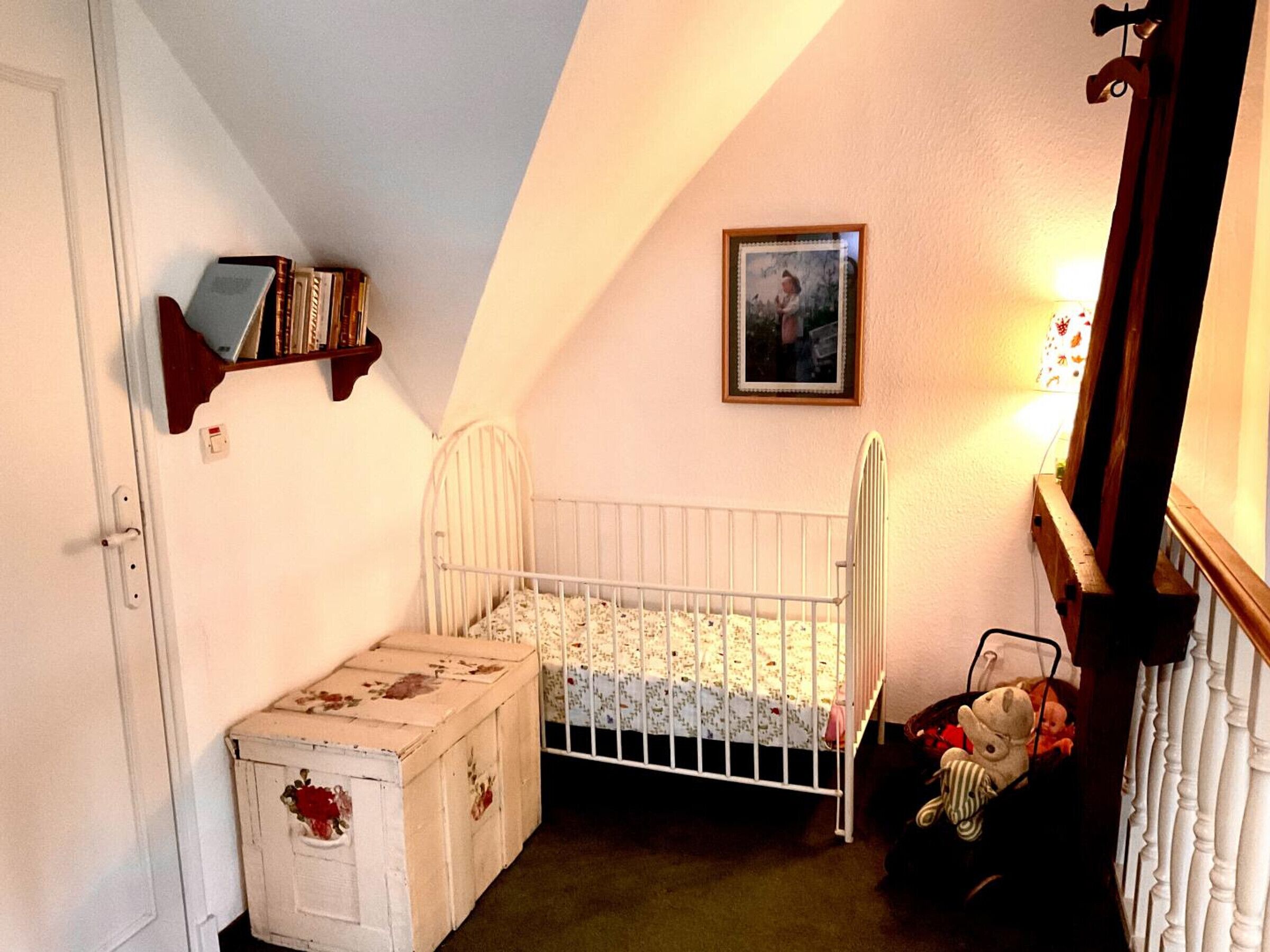 A cozy, well-lit nursery with a white crib, a small chest of drawers, a bookshelf, and a framed picture on the wall.