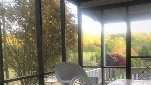 Uma área de estar coberta ao ar livre, com móveis de vime e vista para uma paisagem arborizada.