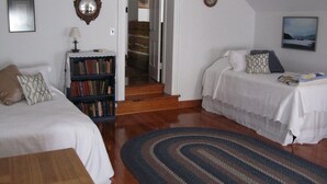 Quarto com duas camas, uma estante de livros, um espelho e uma escada que leva a outro cômodo.