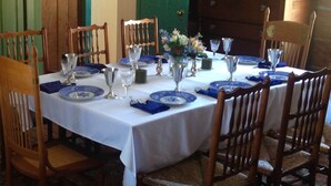 Uma mesa de jantar posta com pratos azuis e brancos, talheres e copos, rodeada por cadeiras de madeira.