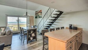 Een moderne keuken met een centraal eiland, een eethoek en een trap naar een balkon met uitzicht.