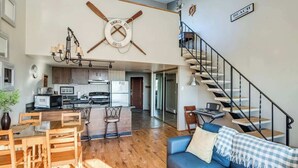 Un salón amplio con una mesa de comedor, un sofá azul, una cocina al fondo y una escalera.