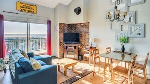 Una sala de estar con sofá, televisión, chimenea, mesa de comedor, sillas y un balcón con vistas.