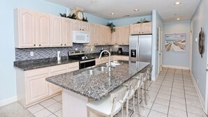 A modern kitchen with light wood cabinets, granite countertops, stainless steel appliances, and a bar area with bar stools. - Desoto unit 302, Luxury 3 Bedroom with Amazing Ocean View  (Tybee Island)