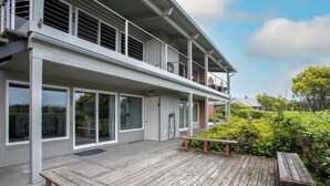 Ein modernes, zweistöckiges Gebäude mit Balkon, großen Fenstern und einer Holzterrasse.