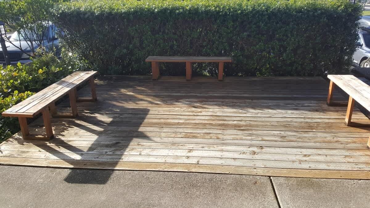 A wooden deck with two benches and a hedge in the background.