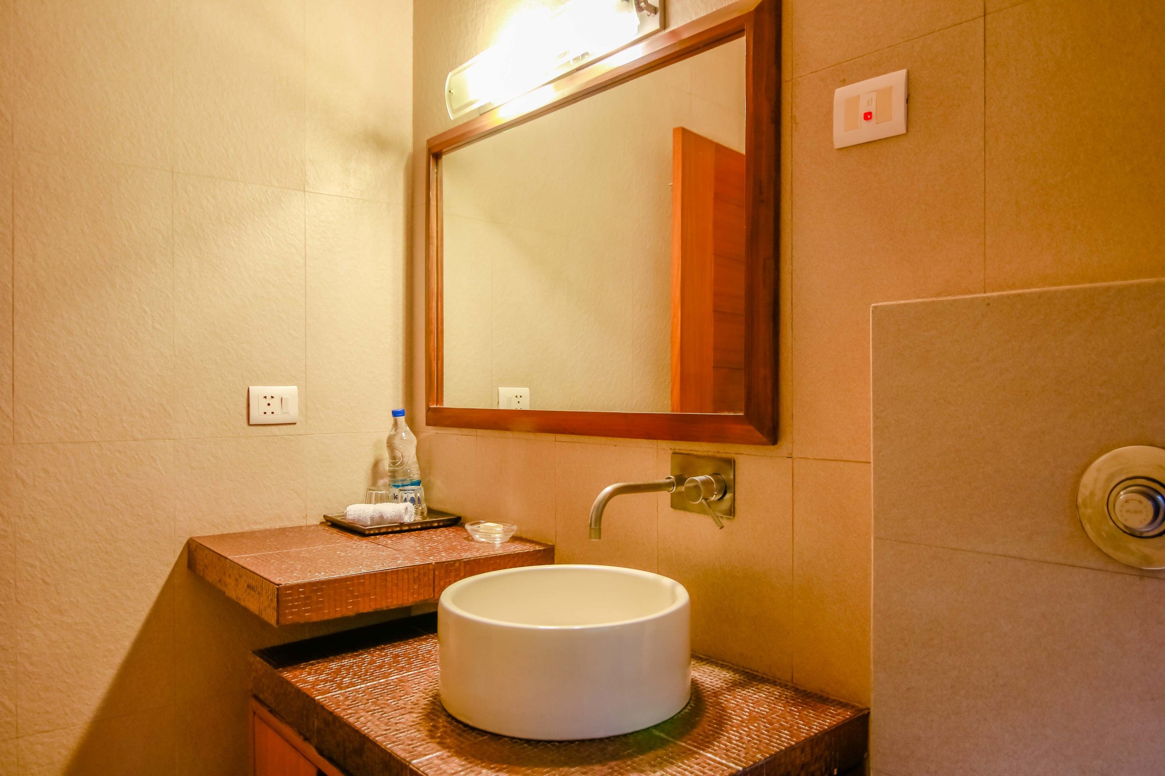 A bathroom with a round white sink, a wooden countertop, a mirror, and a light fixture above the mirror.