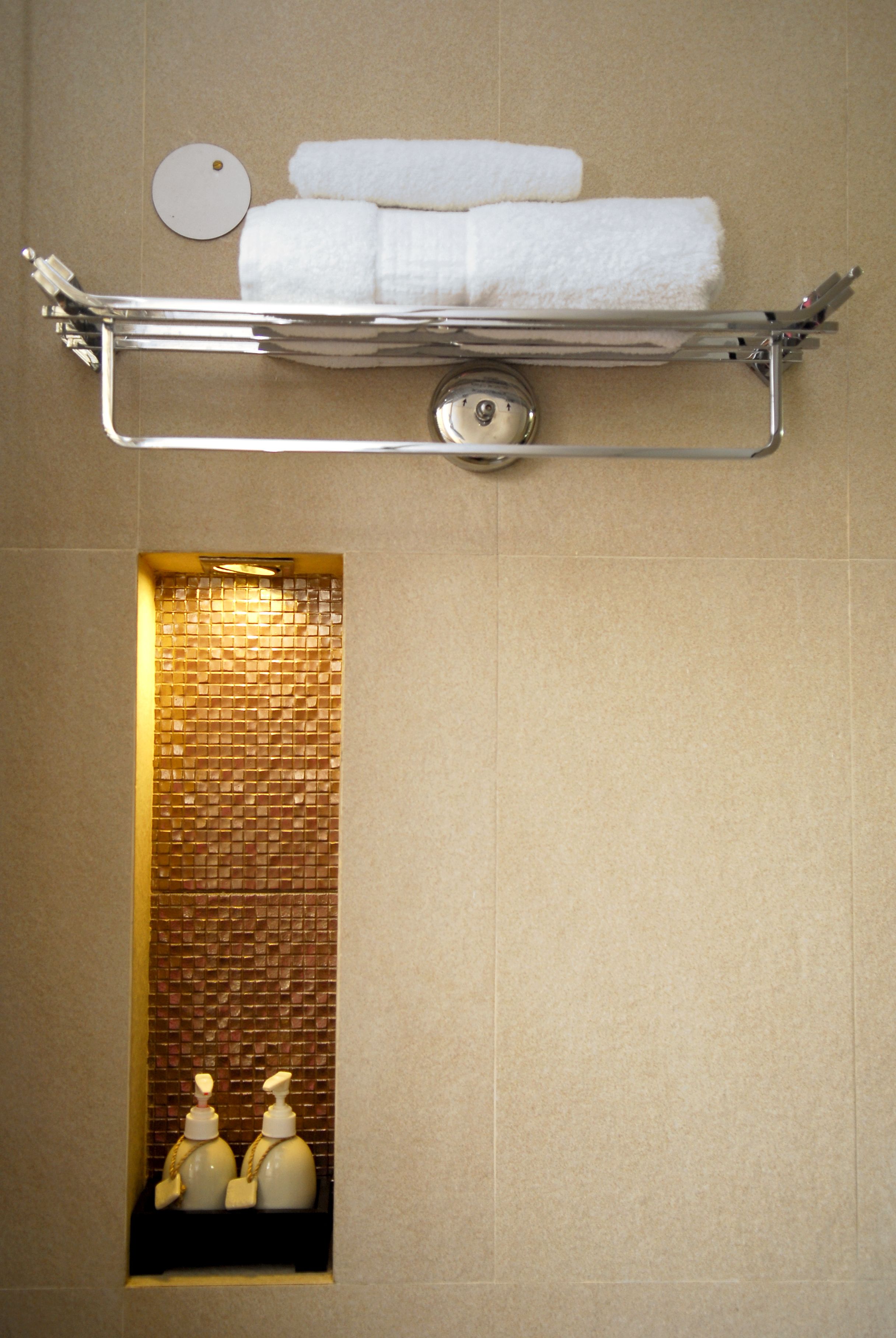 Une salle de bain équipée d’un porte-serviettes sur lequel sont pliés deux serviettes, d’un miroir rond et d’un distributeur de savon fixé au mur.