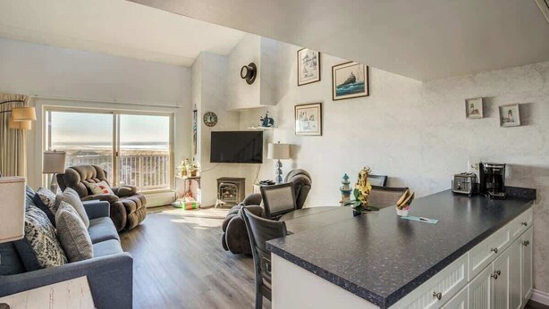 A modern living room with a sofa, a dining area with a kitchen island, a TV, and a fireplace.