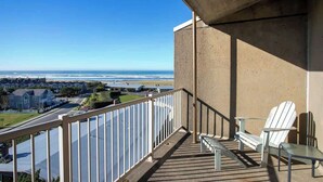 A balcony with a view of the ocean, two Adirondack chairs, and a concrete wall.