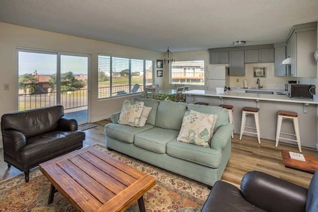A living room with a sofa, coffee table, and a dining area with a kitchen in the background.