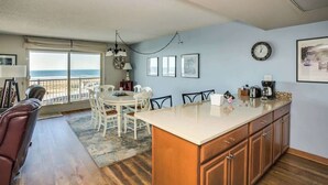 Une cuisine dotée d’un grand îlot central, d’un coin repas avec des chaises, d’un canapé et d’une vue sur l’océan.