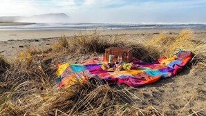 Un coin pique-nique aménagé sur la plage avec une couverture, un panier et de la nourriture.
