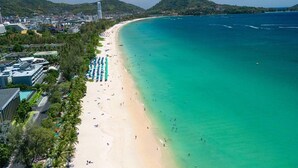 A beach with clear turquoise waters, a sandy shore, and a row of umbrellas. - The Nature Phuket (Patong)