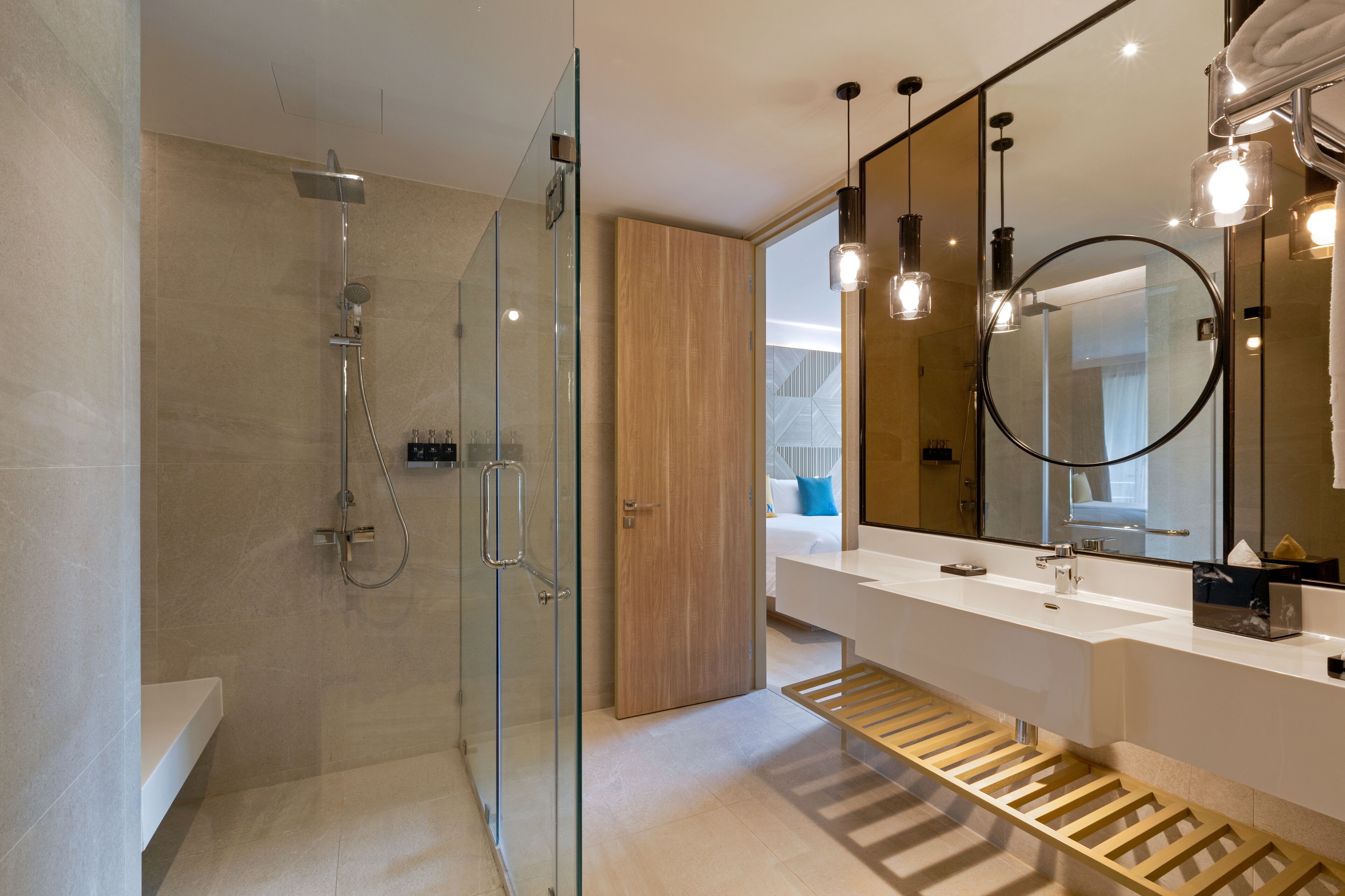 A modern bathroom with a glass shower enclosure, a wooden door, a large mirror, and a wooden vanity.