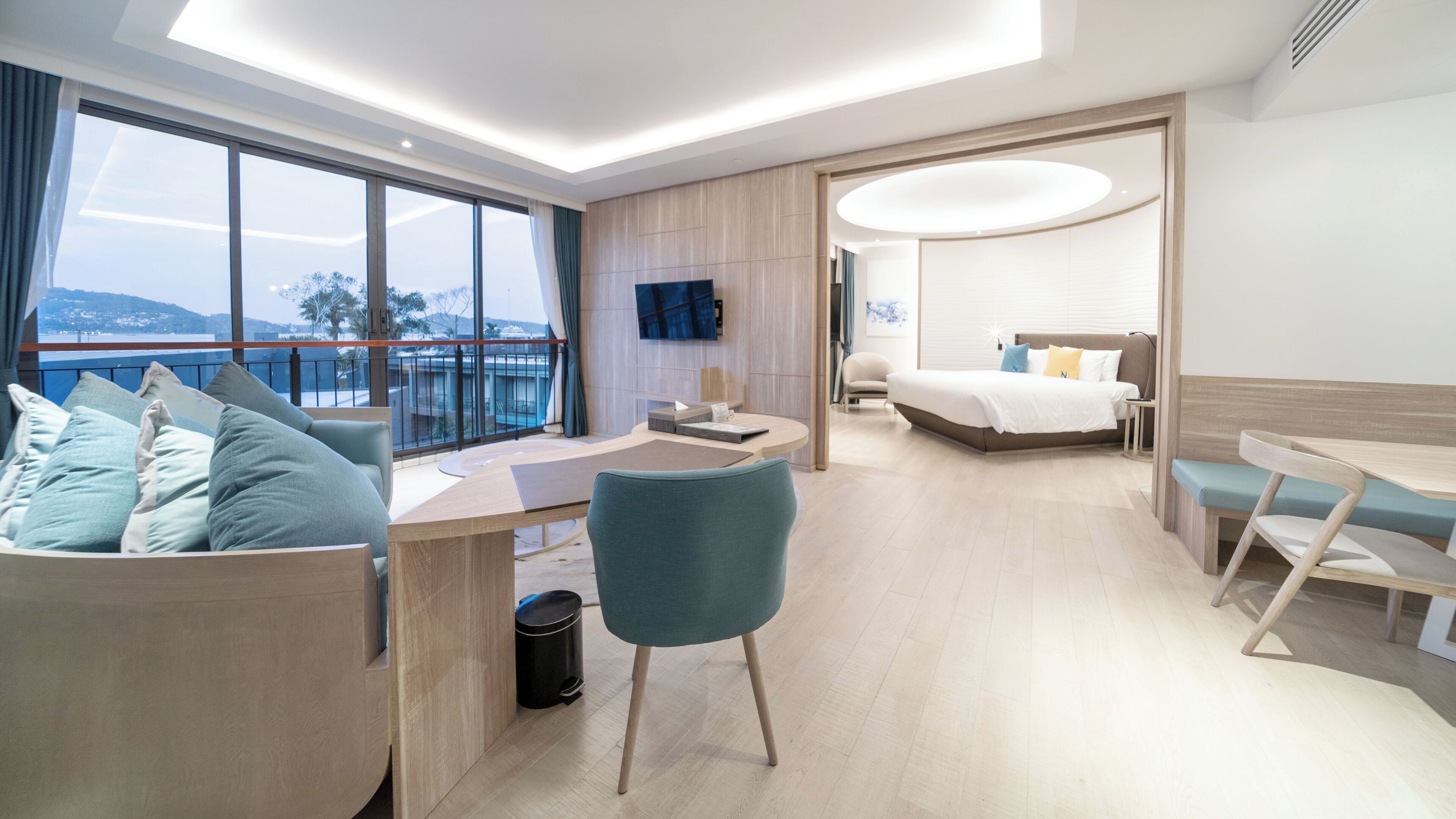 A modern hotel room with a balcony, a desk, a chair, a bed, and a TV.
