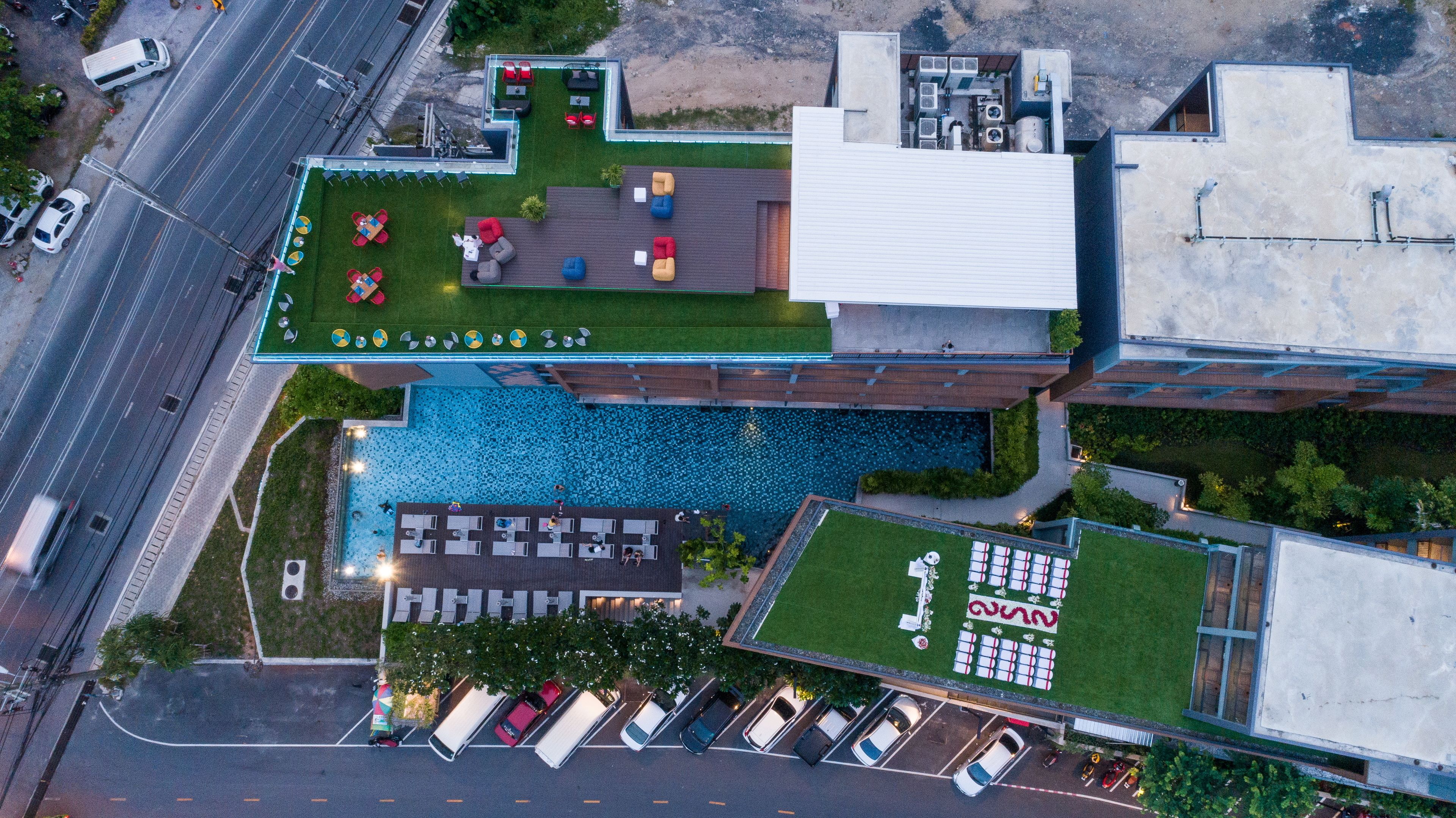 An aerial view of a modern building with a rooftop pool, outdoor seating area, and a parking lot.