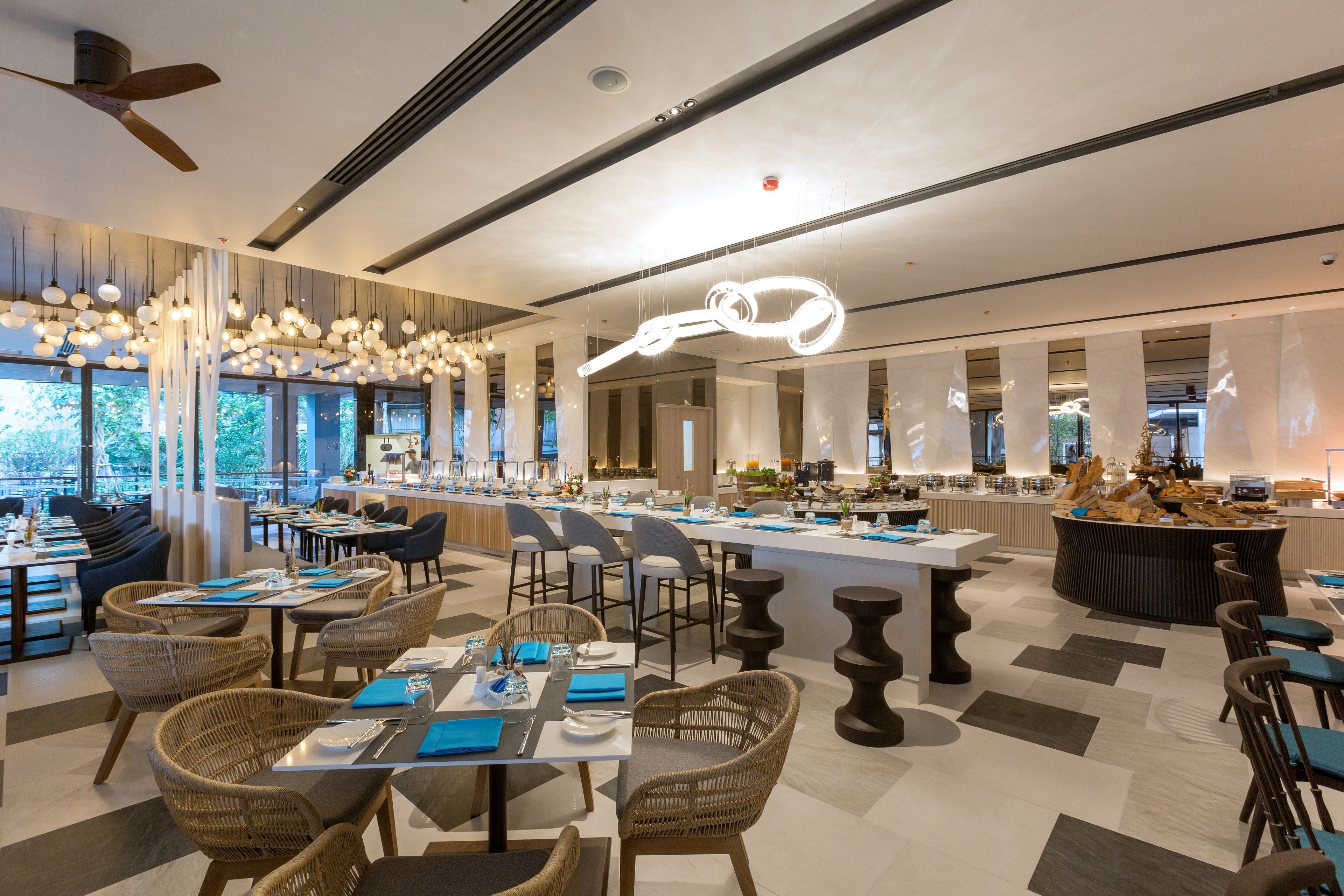 A modern restaurant with high ceilings, pendant lighting, and a central island. Tables are set with blue napkins and silverware.