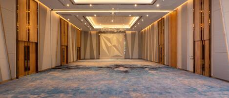 Un long couloir étroit, typique d’un hôtel, avec un tapis bleu, des murs recouverts de panneaux de bois et un plafond orné de luminaires hexagonaux.