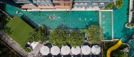 An aerial view of a rooftop pool with clear water, surrounded by greenery and umbrellas.
