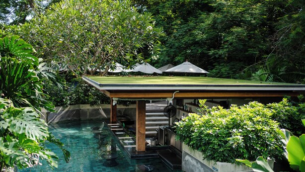 A swimming pool with a covered area, surrounded by lush greenery and a staircase leading to a roofed section. - The Nature Phuket (Patong)