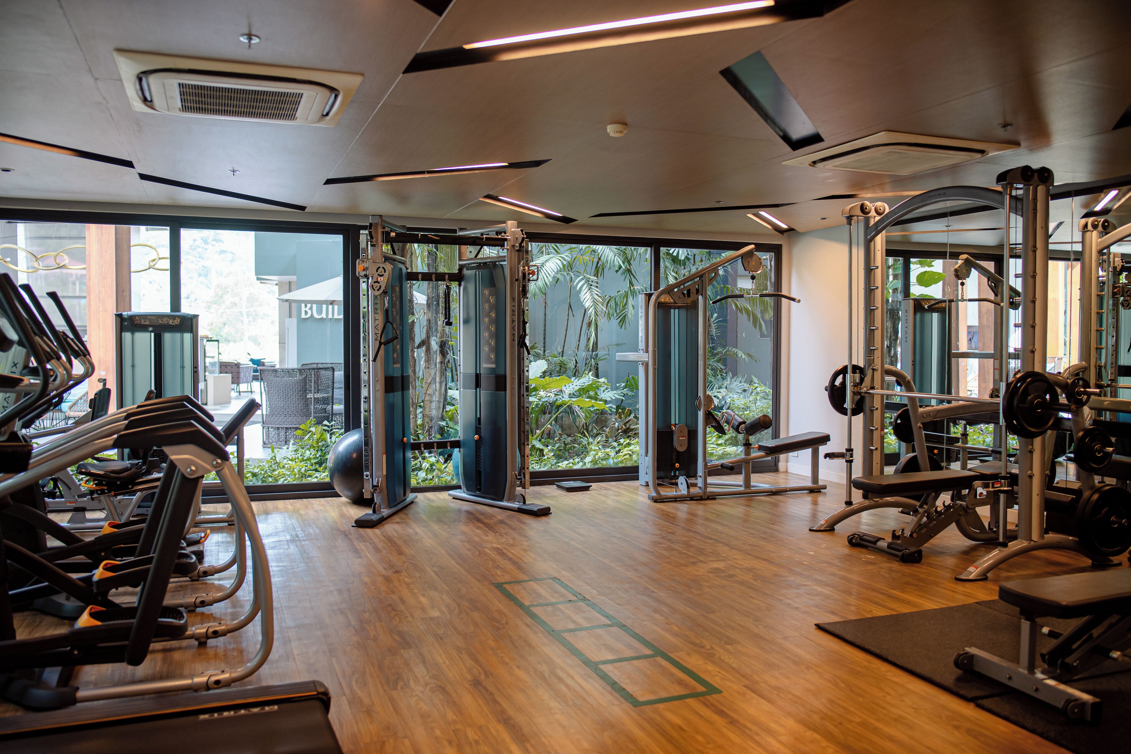 A gym with treadmills, weight machines, and a view of greenery outside.