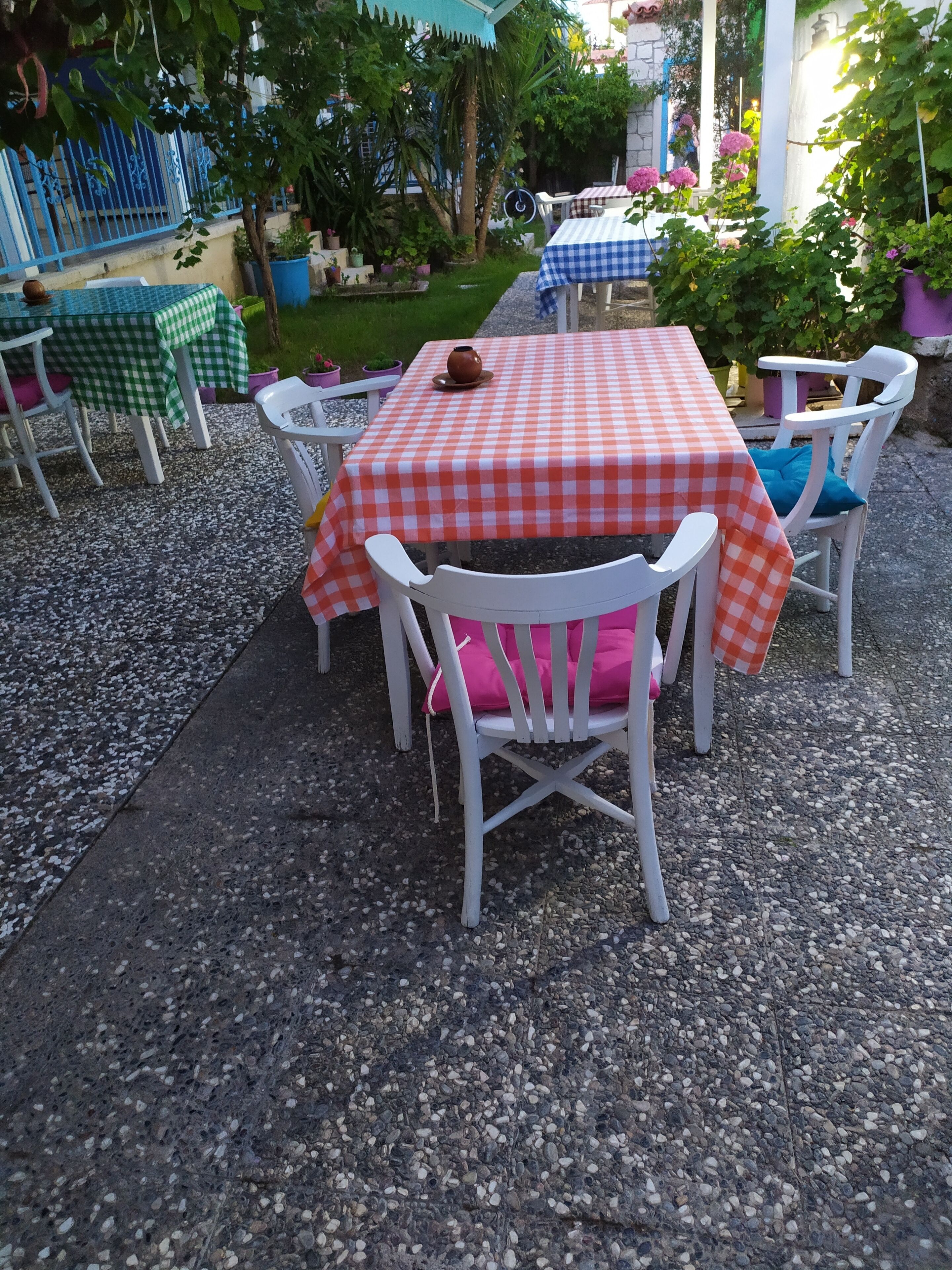 An outdoor patio with a checkered tablecloth, white chairs, and a small garden area.