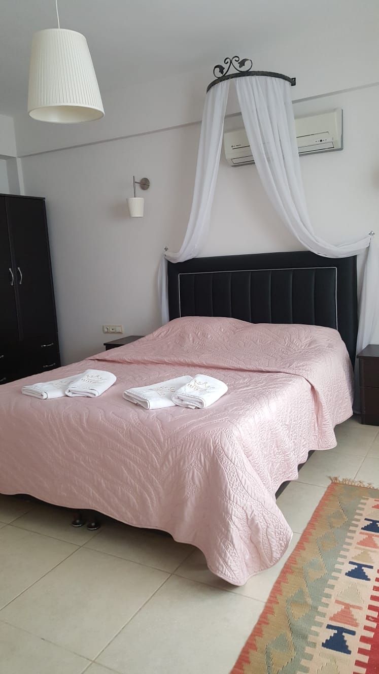 A bedroom with a bed, a nightstand, a wardrobe, a hanging light fixture, and a wall-mounted air conditioner.