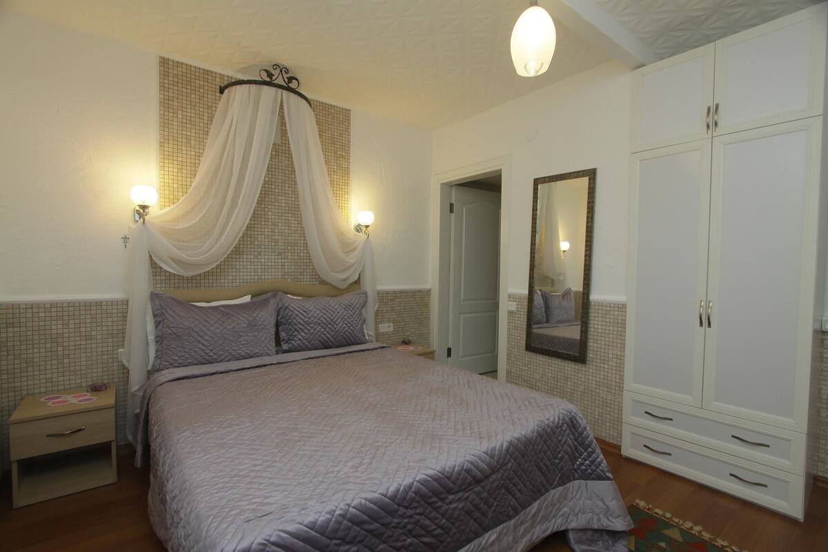 A bedroom with a large bed, a nightstand, a wardrobe, and a mirror on the wall.