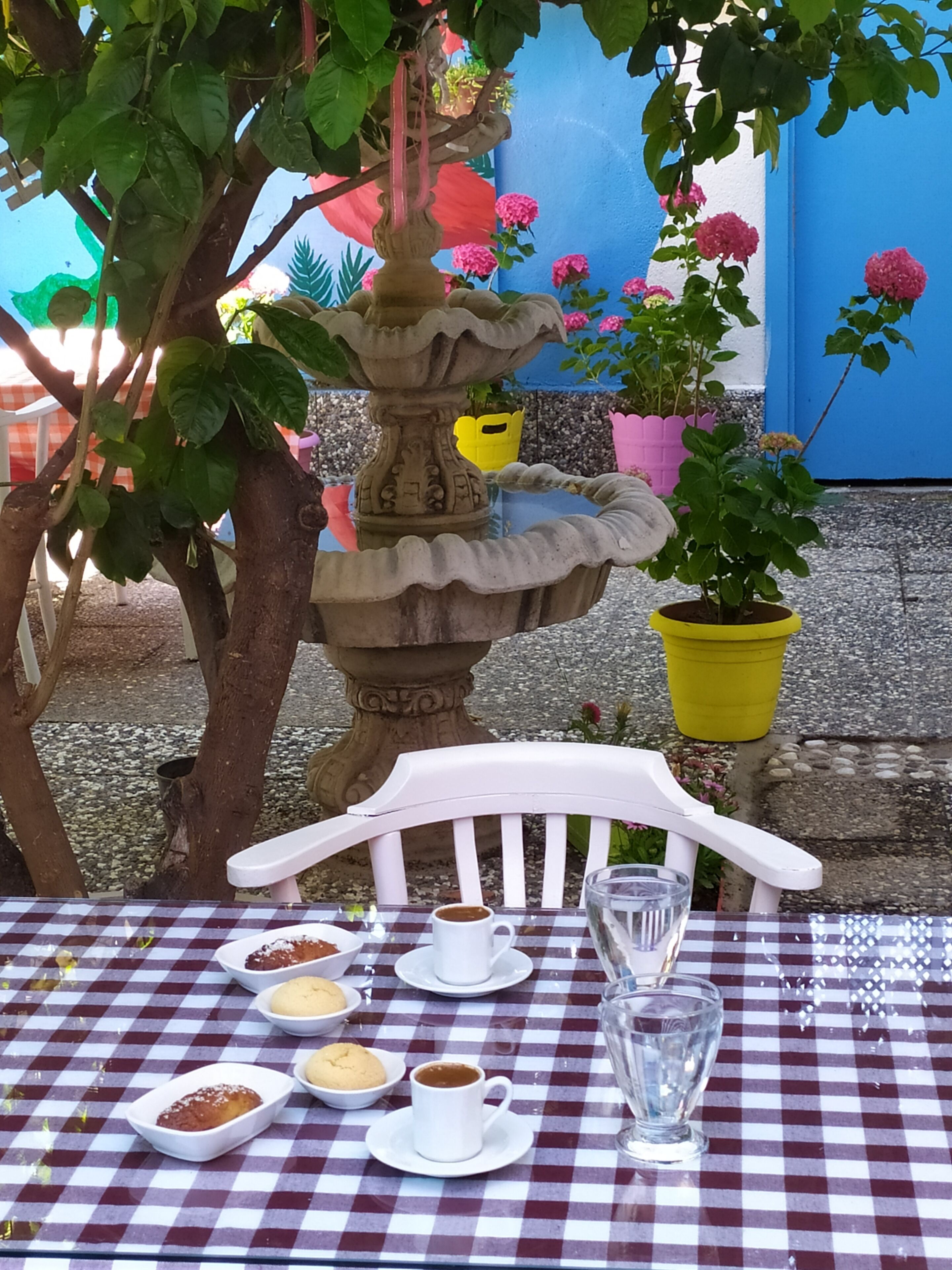 A table set with a checkered tablecloth, a white chair, a glass of water, and a cup of coffee.