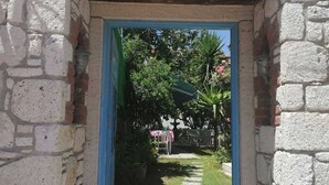 A stone archway with the sign "NANO OTEL" above it, leading to a pathway with greenery and a table set up outdoors. - Nano Hotel (Cesme)