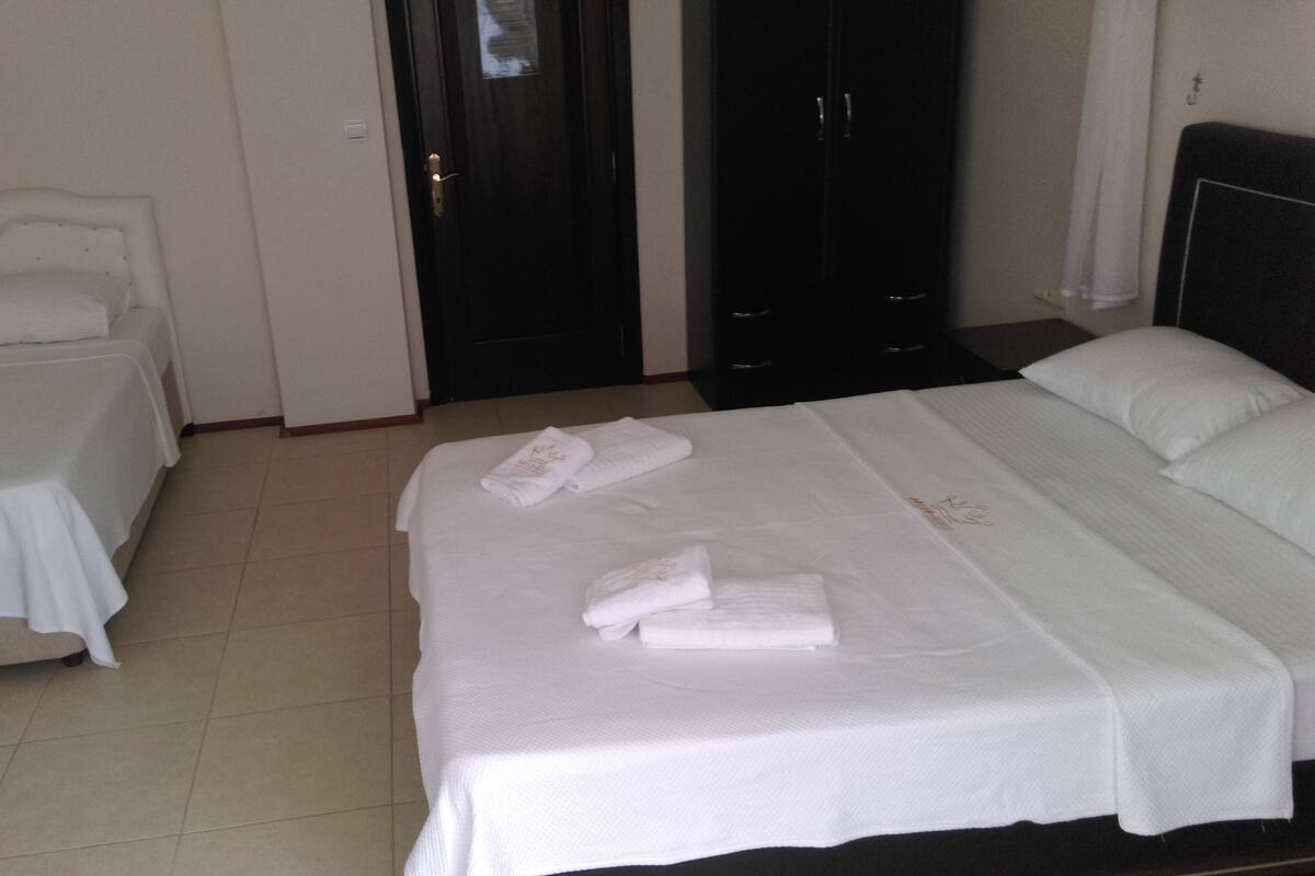 A hotel room with two single beds and one double bed, each with white linens and towels.