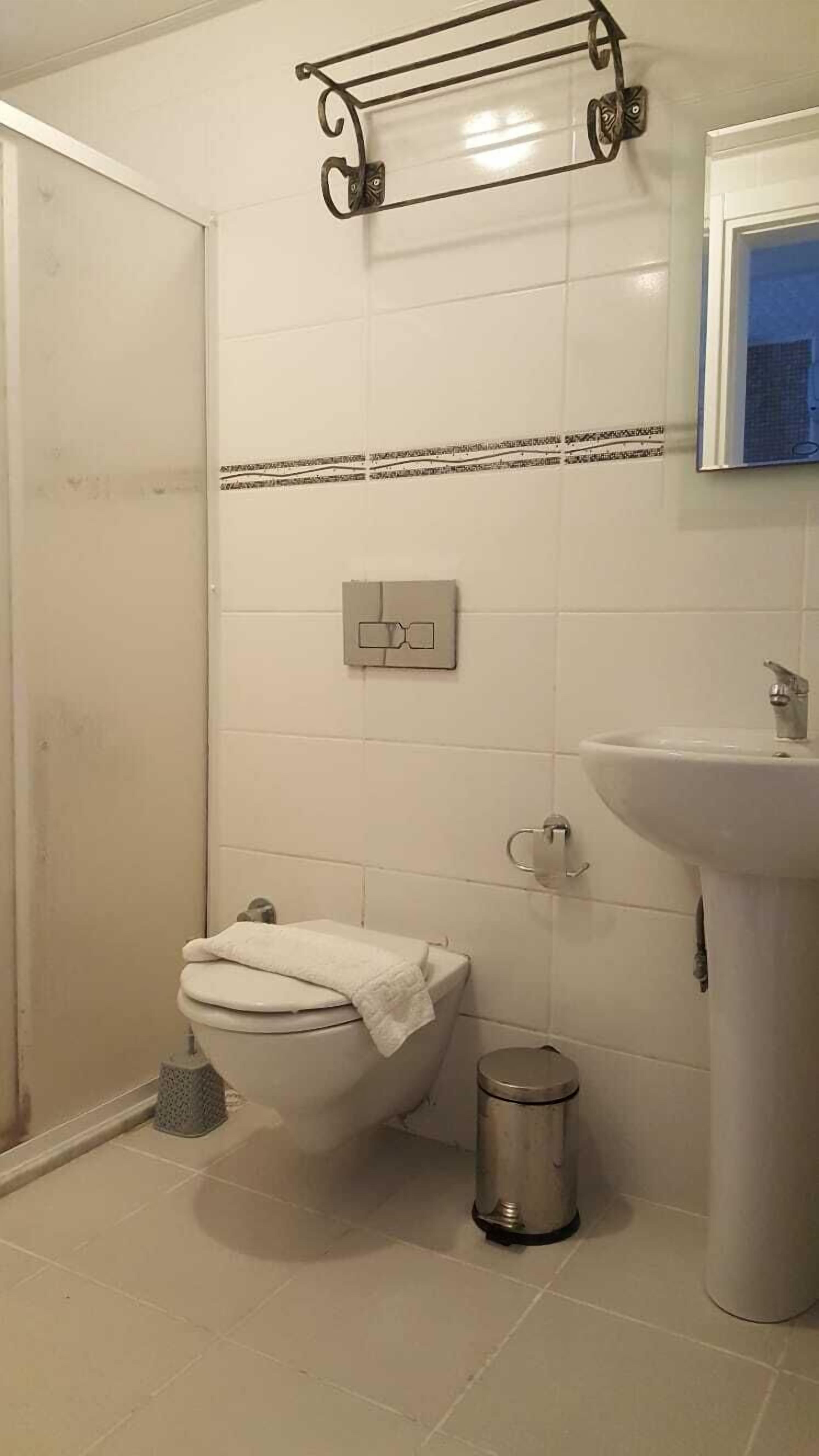 Un baño con inodoro, bidé, lavamanos y un cubo de basura metálico.
