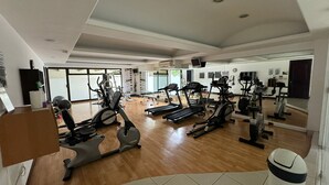 Un gimnasio espacioso con distintas máquinas de cardio, un espejo grande y un ventanal que proporciona luz natural.