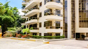 Un hotel de varios pisos con balcones, zona de estacionamiento y áreas verdes.