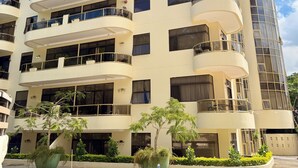 Un edificio de varios pisos con balcones, un estacionamiento y cielo despejado.