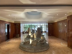 Un hall d’entrée spacieux agrémenté d’une fontaine centrale en pierre, de lambris en bois et de grandes fenêtres laissant entrer la lumière naturelle.
