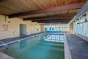 Ein Hallenbad mit Holzbalkendecke, einem blauen Rettungsschwimmerstuhl und Blick durch große Fenster.