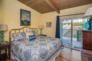 Ein Schlafzimmer mit einem Bett, zwei Nachttischlampen, einem Gemälde eines Schiffes, einer kleinen Fisch-Kunst und Blick auf einen Balkon.