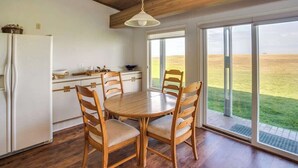 A kitchen with a dining table and chairs, a refrigerator, and a large window with a view of a grassy field.