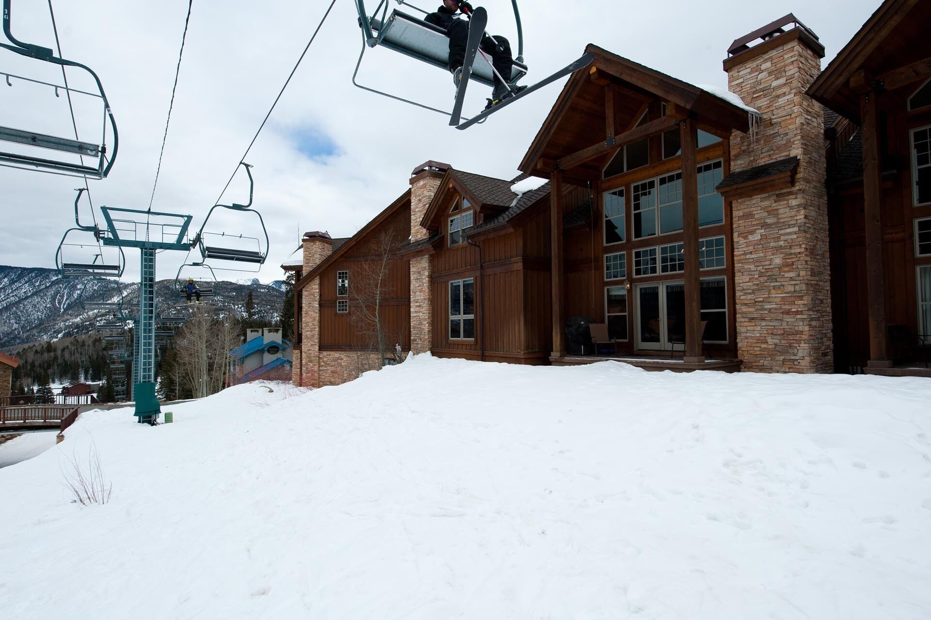 A ski resort lodge with a stone facade, large windows, and a ski lift in the background.