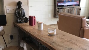 A rustic wooden bar with two stools, a television displaying a news program, and a Buddha statue.