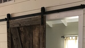 A room with a rustic wooden barn door leading to a bedroom with a bed, a nightstand, and a lamp.