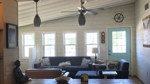 A cozy interior with a wooden dining table, bar stools, a sofa, and a ceiling fan.