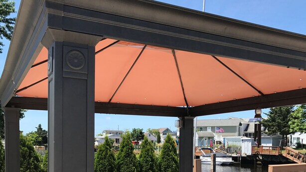 A covered outdoor seating area with a pergola, wicker furniture, and a view of a marina.