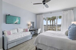A bedroom with a bed, a desk, a chair, a ceiling fan, and a view of palm trees. - Guest Favorite| Gulf Front | Accommodates 12 |  Beach Serv. I Pet Friendly| (Miramar Beach)